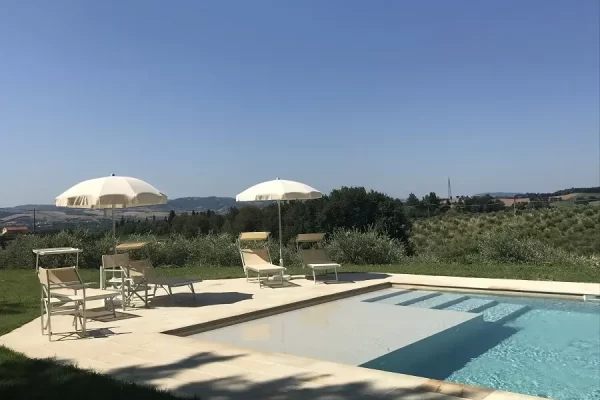 Piscina all'aperto con sdraio e ombrelloni in un paesaggio collinare.